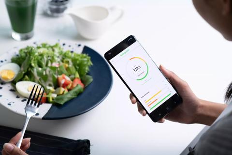 Person monitoring nutritional intake on smartphone app while eating a salad