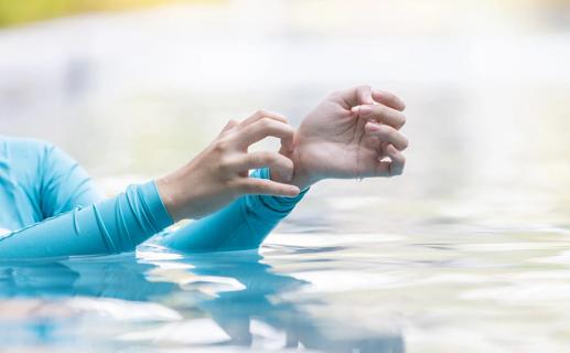 Person in long-sleeve swimwear, scratching at their itchy wrist