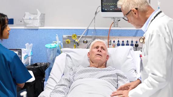 Doctor and hospital tech standing next to an older patient in a hospital bed