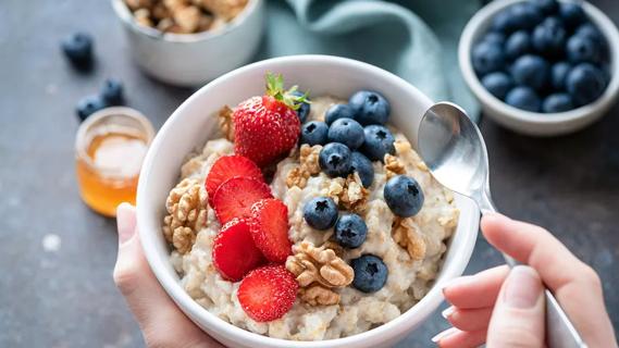 Hand holding bowl of oats with honey, strawberries, blueberries and walnuts