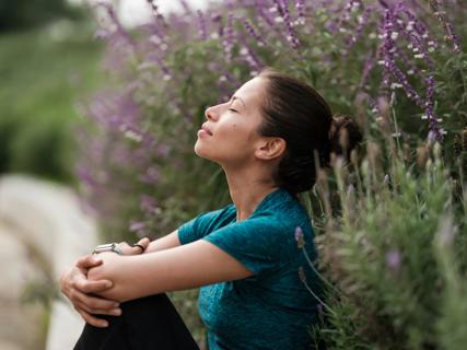 Person relaxing, head back, eyes closed, sitting in patch of purple flora