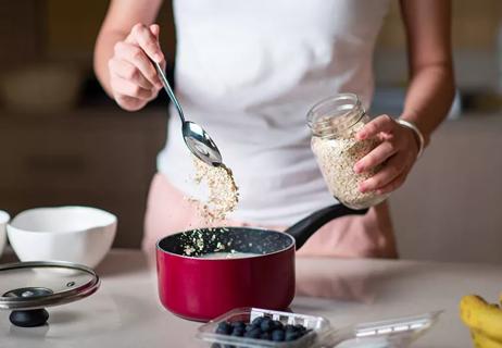 Person spooning rolled oats into a kitchen pot as part of meal prep