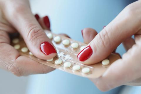 Hands with red polished nails holding a packet of contraceptive, birth control pills