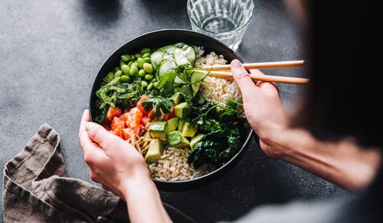 Person about to eat a bowl of rice and mixed veggies, including edamame, sprouts and avocados