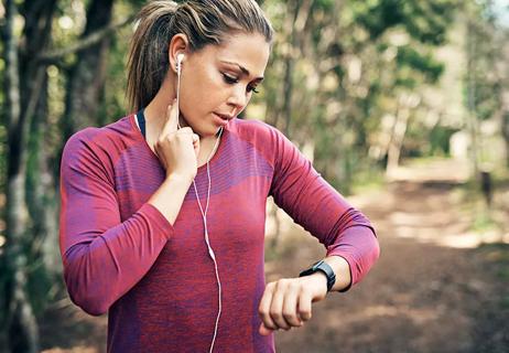 Woman feeling for heart rate in neck on run outside, smartwatch and earbuds