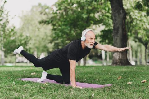 Older person doing dog bird yoga pose on exercise mat outside