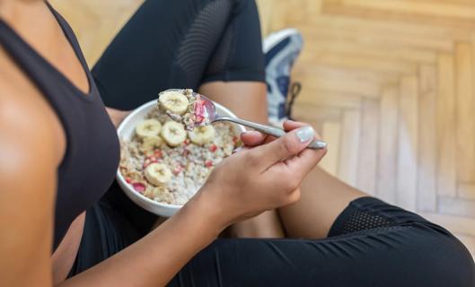 Person in workout clothes, eating bowl of oatmeal, berries and bananas