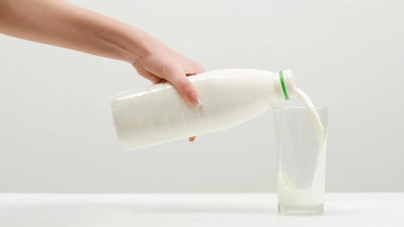 Hand pouring milk from a glass bottle into a glass