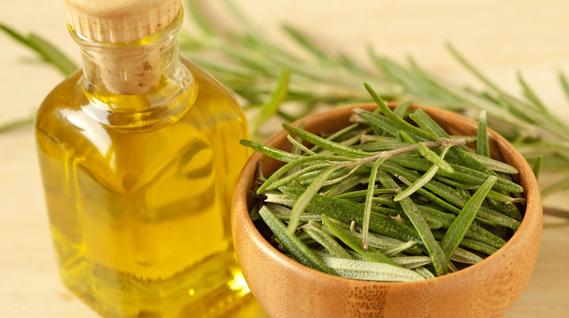 Rosemary oil in glass bottle and fresh rosemary in wooden bowl