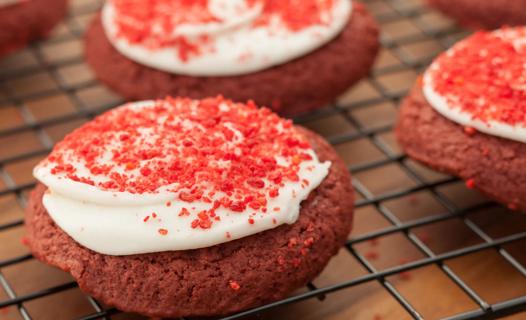 Freshly baked and frosted red velvet cookies on a cooling rack