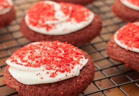 Fresh baked cookies using red dye with white frosting and red sprinkles