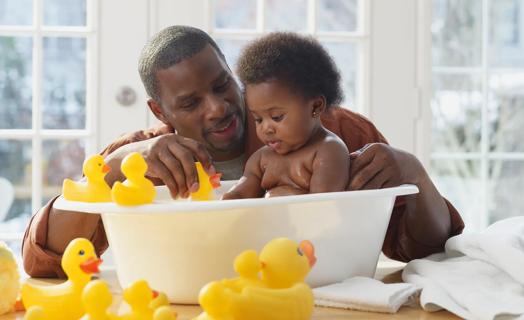 Caregiver giving young toddler a bath in plastic baby tub, with rubber duckies all around