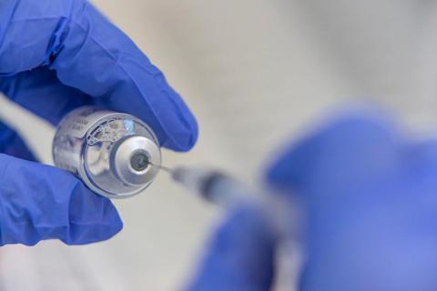 Gloved hands of healthcare provider inserting syringe into vial of vaccine
