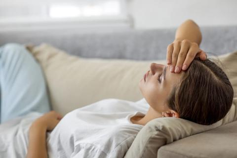 Person lying on couch, with a hand across their forehead and a hand on their stomach