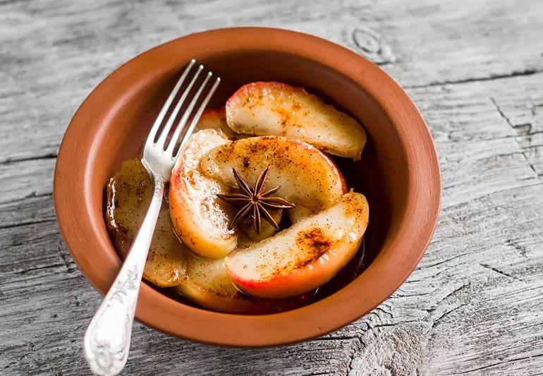 Baked cinnamon apples in a brown bowl on a grey wooden tabletop.