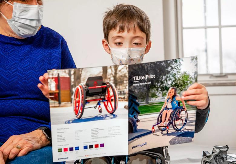 A child wearing a mask looks at a brochure about using a wheelchair