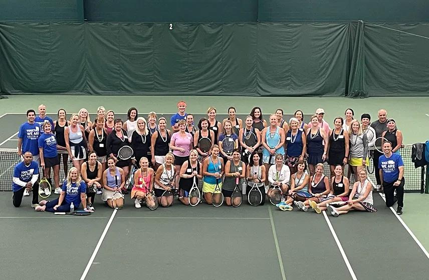 Group of tennis players pose on an indoor court during a community fundraising event.