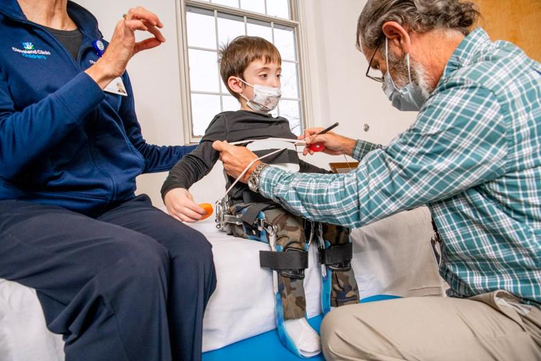 An adult straps a child into a chair so he can sit up