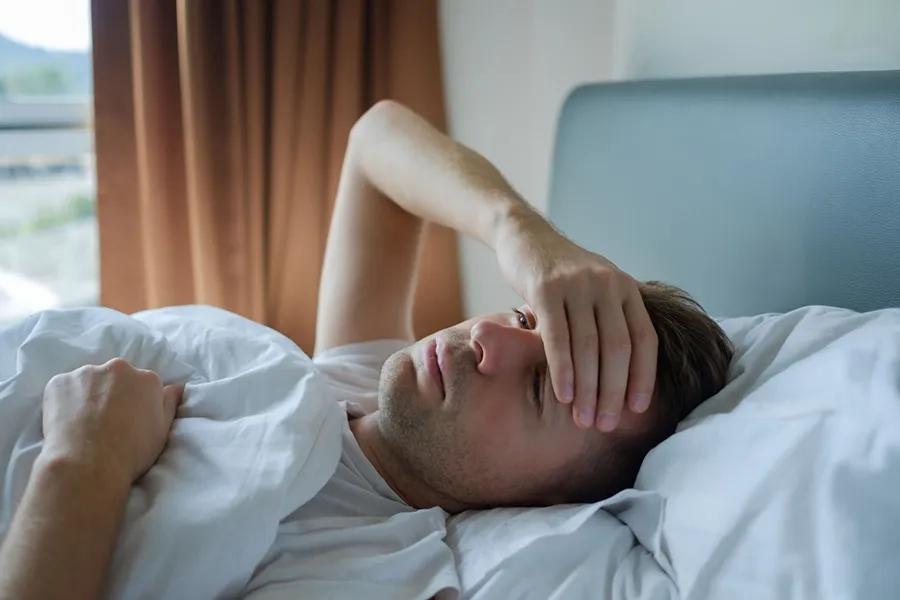Person lying in bed with hand on their forehead.