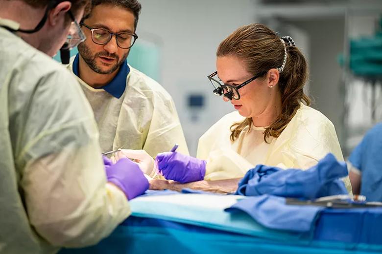 A surgeon sits next to a student to teach a surgical technique