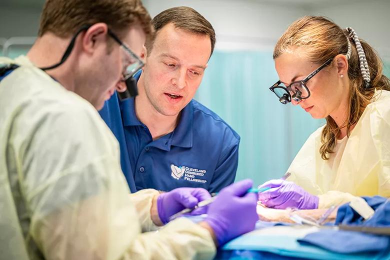 A surgeon sits next to students practicing surgical skills