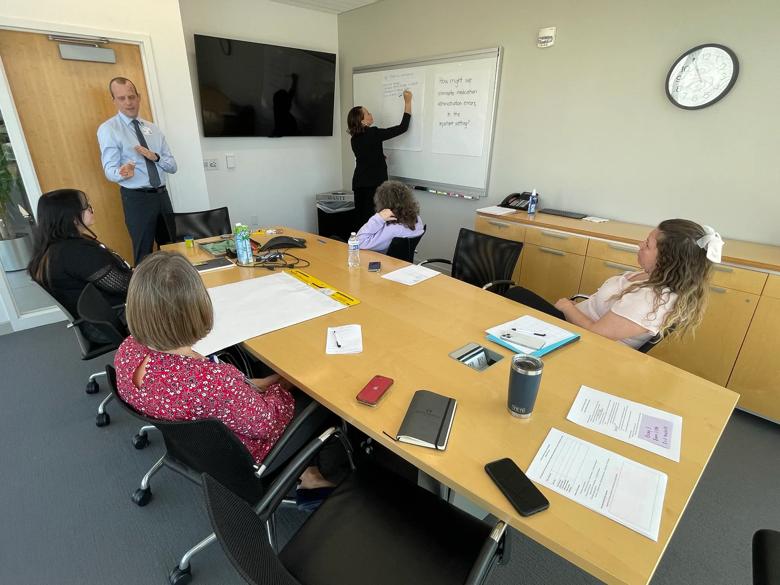 An image of a breakout session. People are looking at someone writing their ideas on a whiteboard.