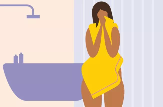 Person standing in front of bathtub, drying off with towel