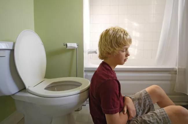 Person sitting by toilet in bathroom, holding stomach