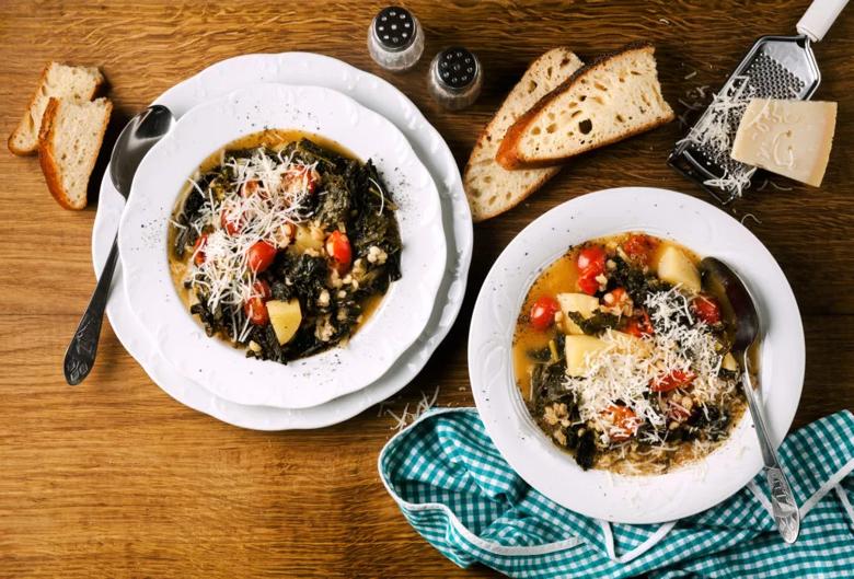 Two bowls of barley soup, with hearty bread and grated cheese on table