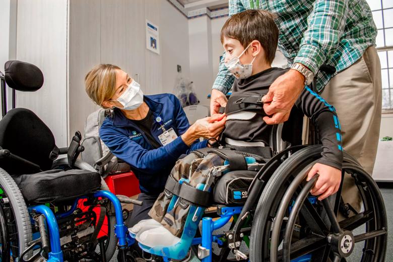 A woman in a blue shirt checks on a child buckled into a wheelchair