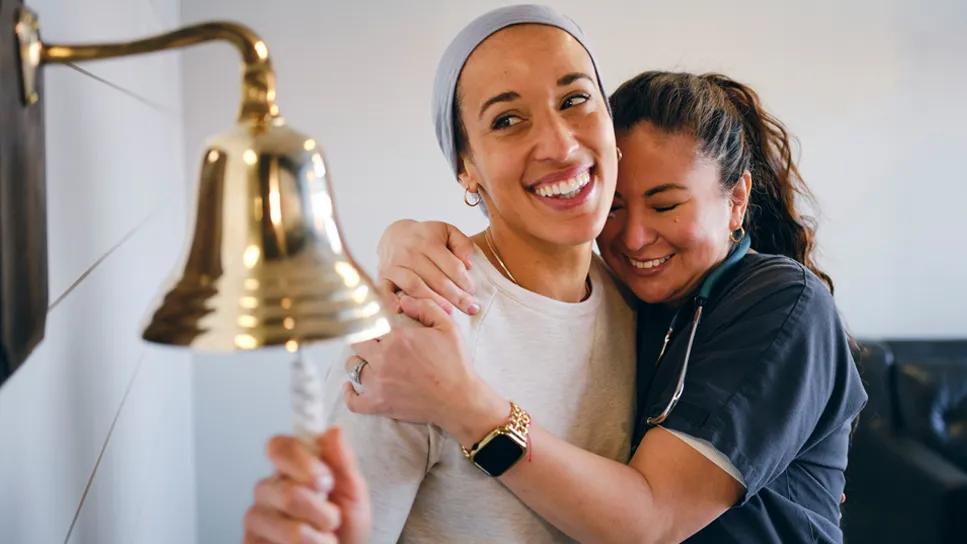 Visibly wearing a scarf to cover her head, a woman rings the bell following chemo treatment.
