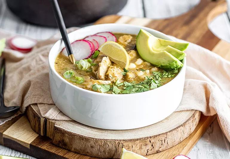 A cup of the traditional Mexican soup pozole with chicken, avocado slices and radishes