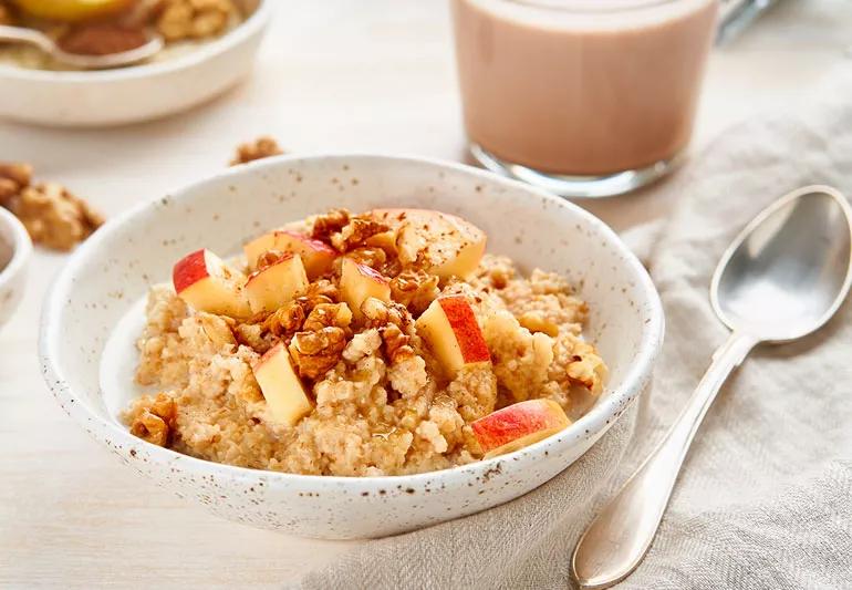 recipe steel cut oatmeal with apples and walnuts in a white bowl on a beige tablecloth.