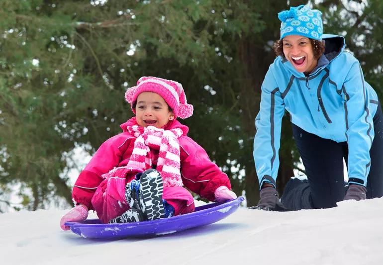 mom and daughter sledding during winter