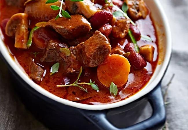 A bowl of stew made of carrot slices, mushrooms and chunks of beef