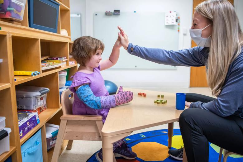 Little girl sitting in a chair gives a high five to an adult